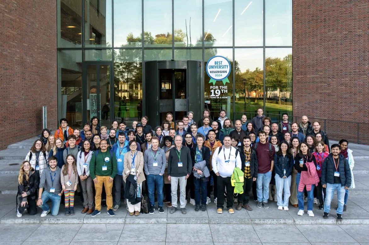 Large group of people wearing badges standing together outside a modern university …